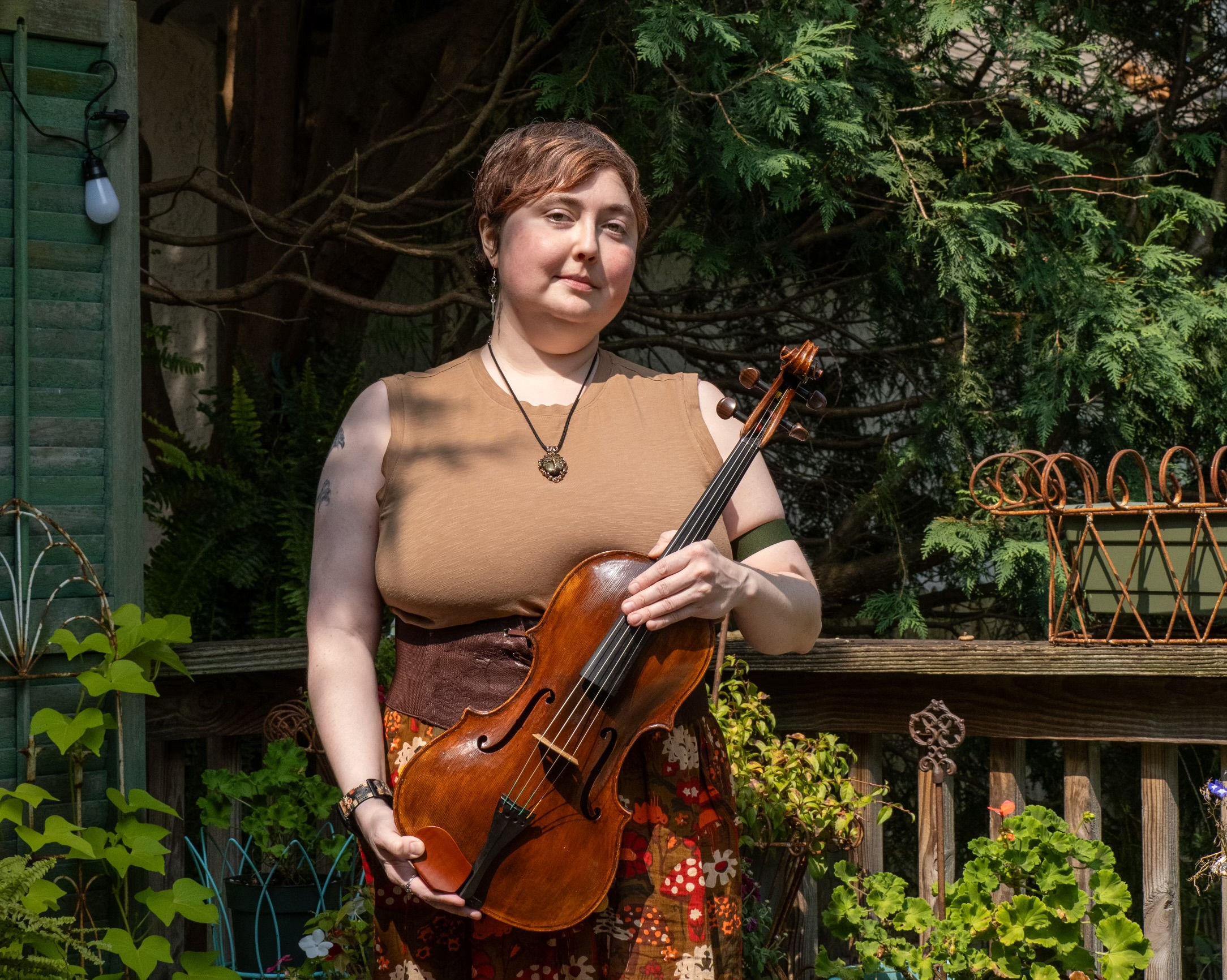 Hannah Barton holds her violin outdoors, with plants in the background